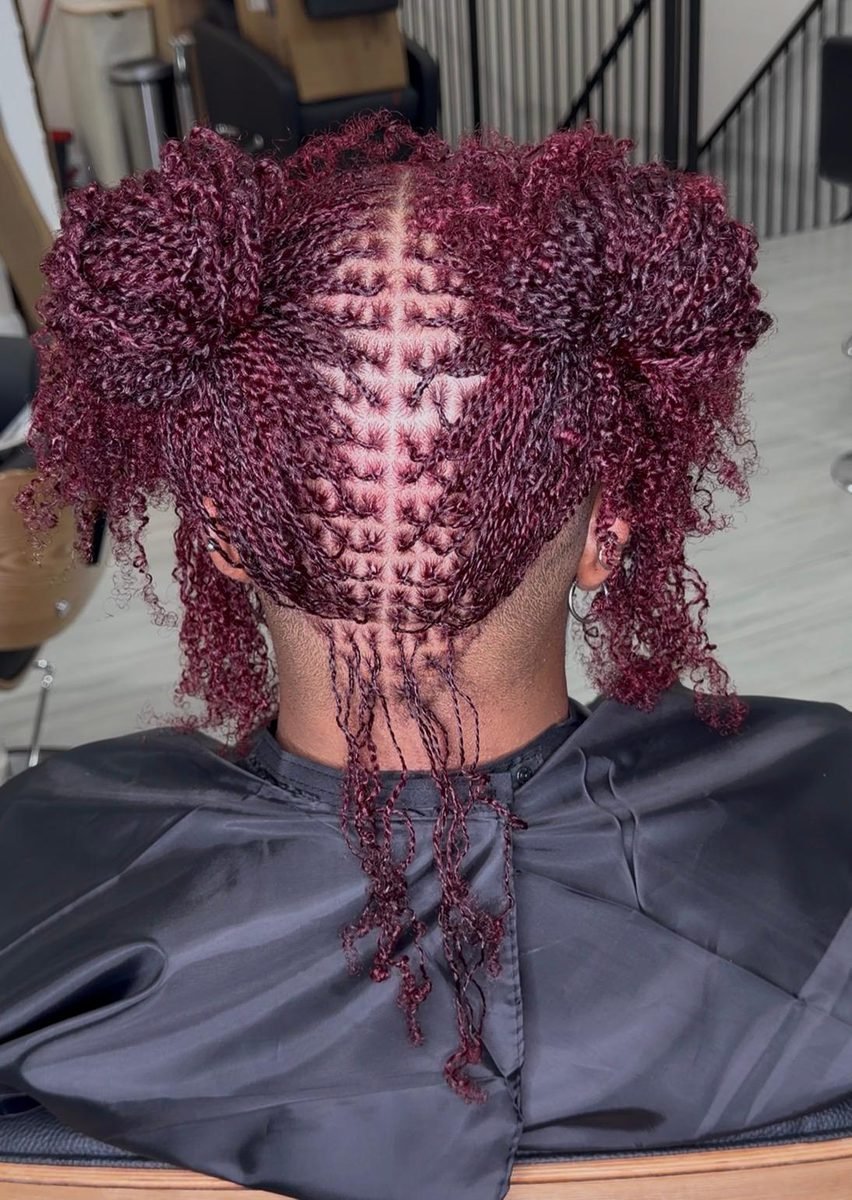 Client with burgundy colored locs styled into symmetric twin puffs
